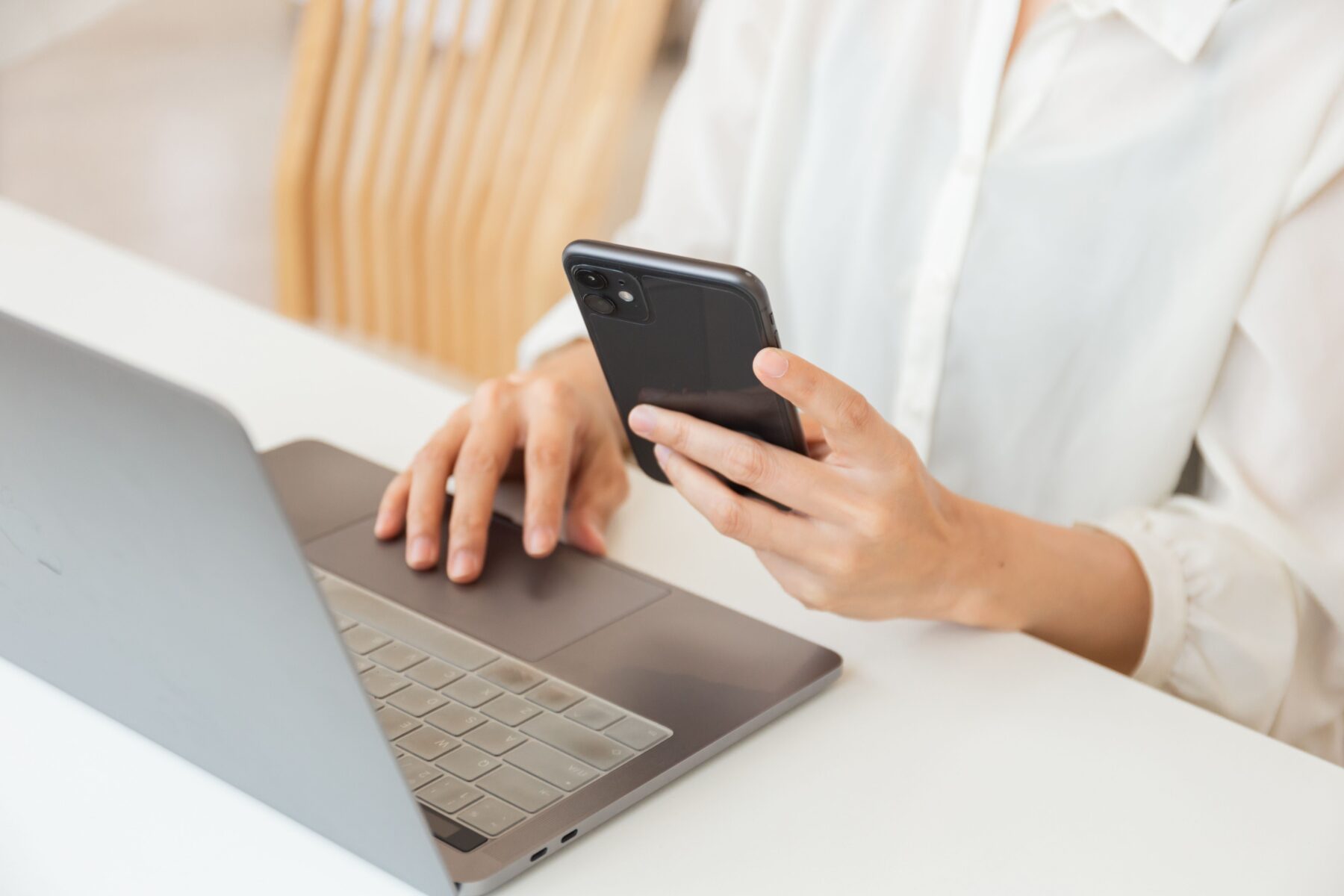 woman holding a phone and typing on a computer at the same time