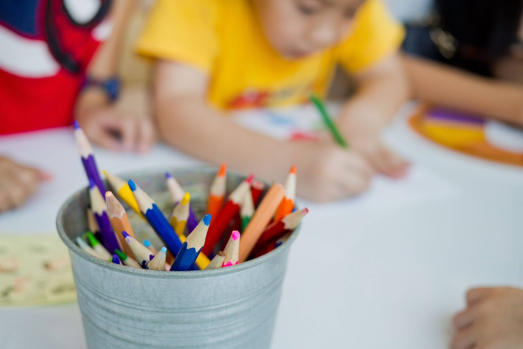 Kids coloring at a table with a bucket of colored pencils
