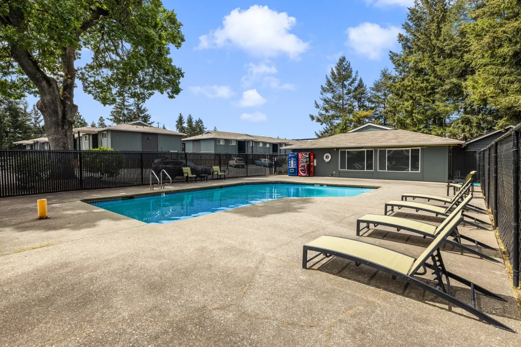 Fenced pool with deck chairs and large trees